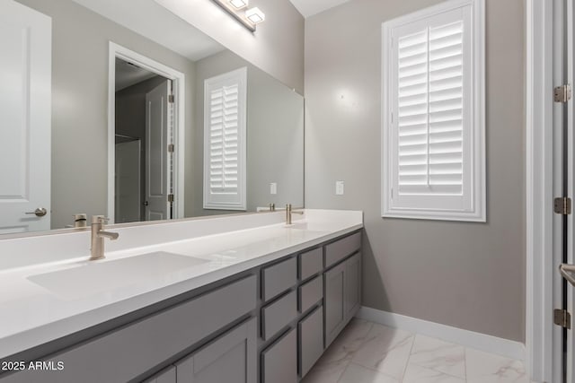 full bathroom featuring double vanity, marble finish floor, baseboards, and a sink