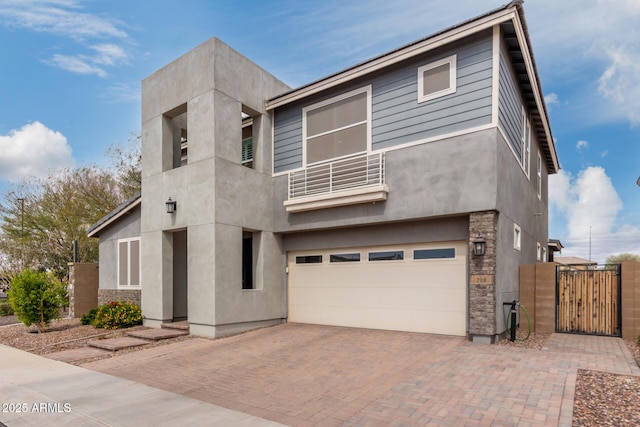 modern home featuring stucco siding, a gate, decorative driveway, a garage, and a balcony