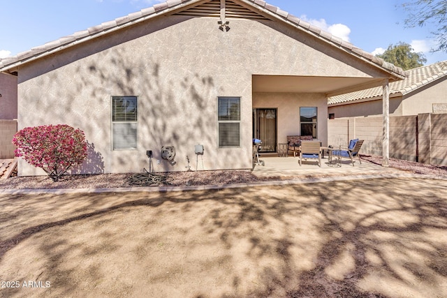 rear view of house featuring stucco siding, a tiled roof, fence, and a patio