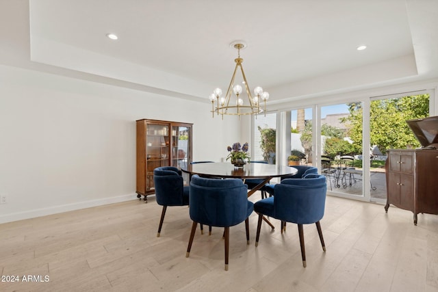 dining area with a tray ceiling, an inviting chandelier, and light wood-type flooring