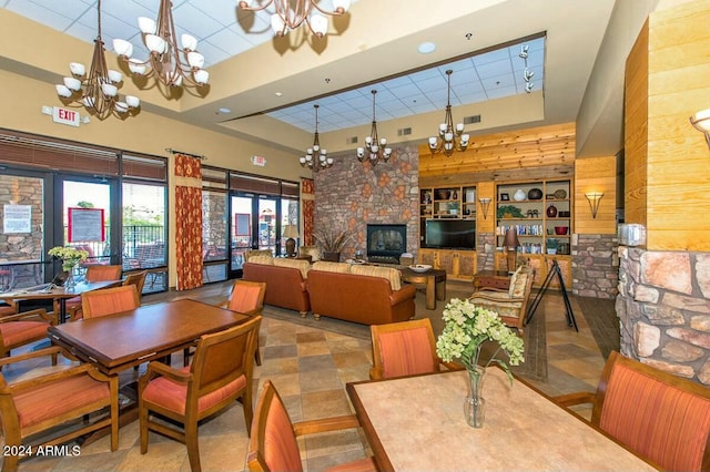 dining space with wooden walls, a notable chandelier, a stone fireplace, and a high ceiling