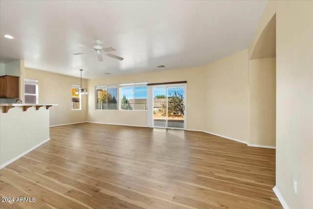 unfurnished living room with ceiling fan with notable chandelier and light wood-type flooring