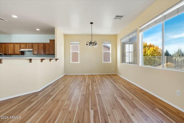 unfurnished dining area with light wood-type flooring and an inviting chandelier