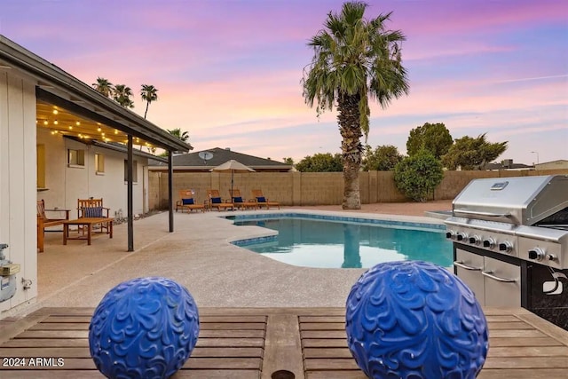 pool at dusk featuring area for grilling and a patio