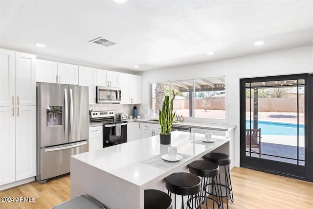 kitchen featuring stainless steel appliances, white cabinetry, light hardwood / wood-style flooring, and a kitchen island