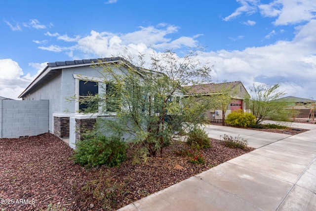 view of home's exterior with stone siding, stucco siding, driveway, and fence