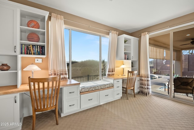 office space featuring a ceiling fan, built in study area, and light carpet