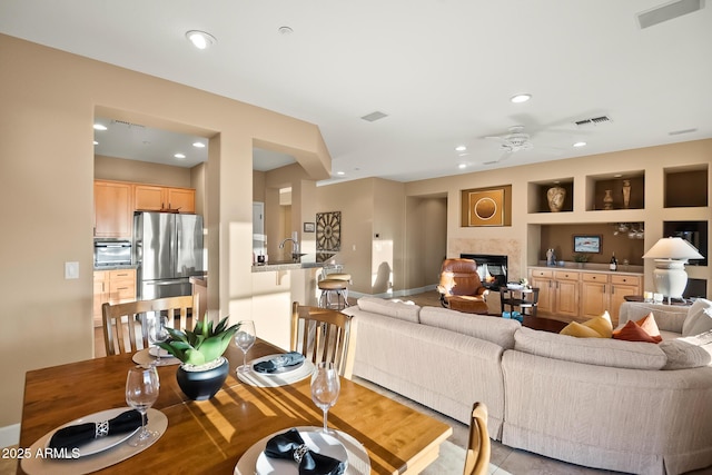 living area with built in shelves, a glass covered fireplace, visible vents, and recessed lighting