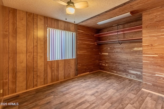 unfurnished room with wooden walls, baseboards, a ceiling fan, wood finished floors, and a textured ceiling