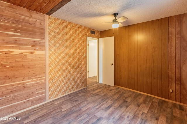 empty room with visible vents, ceiling fan, a textured ceiling, wood finished floors, and baseboards