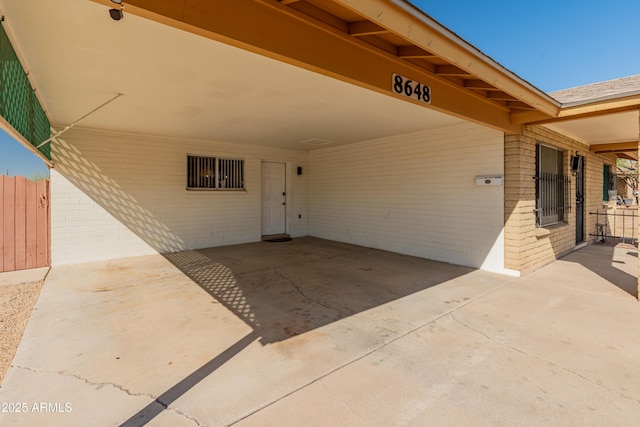 doorway to property with an attached carport, brick siding, fence, and driveway