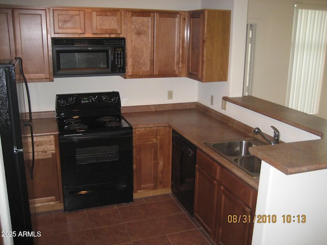 kitchen with brown cabinetry, dark tile patterned flooring, a sink, black appliances, and dark countertops