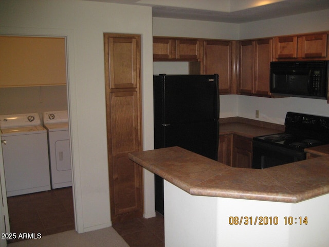 kitchen featuring black appliances, light tile patterned flooring, brown cabinetry, and washer and clothes dryer