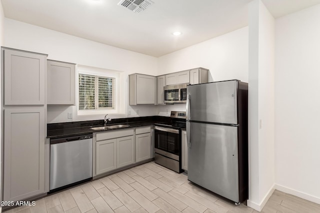 kitchen with stainless steel appliances, sink, gray cabinetry, and light hardwood / wood-style flooring