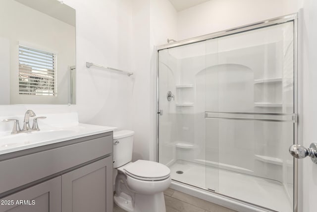 bathroom featuring a shower with door, vanity, and toilet