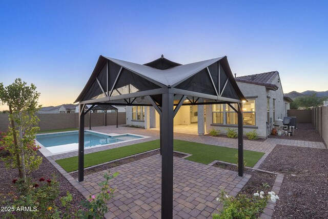 5245 N 205th Ln, Buckeye, AZ 85396 - back of property at dusk featuring a gazebo, stucco siding, a fenced backyard, a tiled roof, and a patio