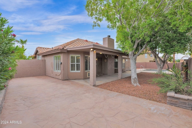 back of house featuring fence, a tiled roof, stucco siding, a chimney, and a patio area