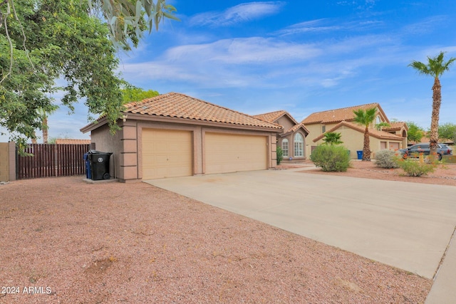 view of front of house with fence, a tile roof, stucco siding, a garage, and driveway