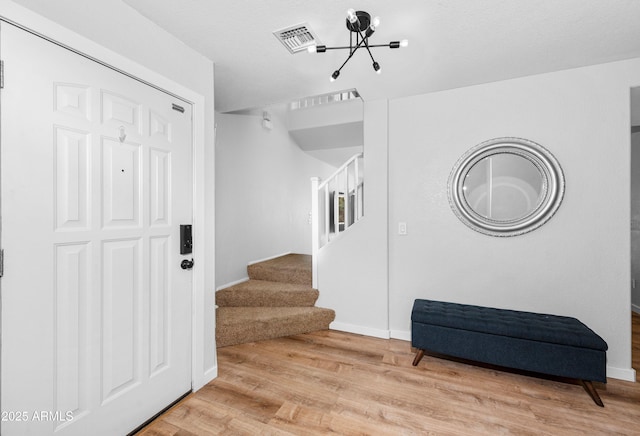 entrance foyer with visible vents, baseboards, stairway, light wood-type flooring, and an inviting chandelier