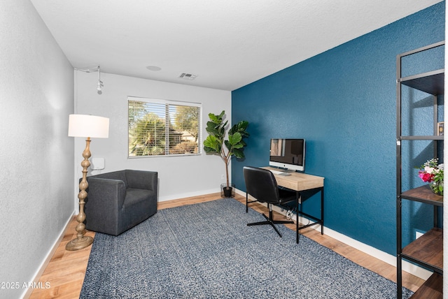 office area featuring a textured wall, wood finished floors, visible vents, and baseboards