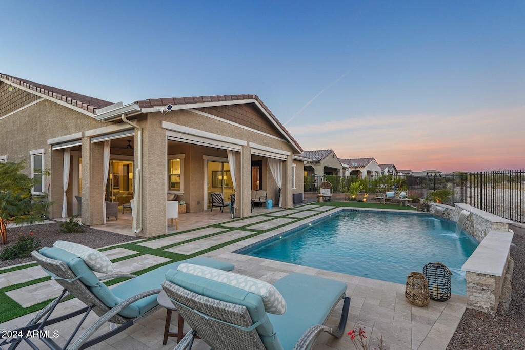 pool at dusk featuring pool water feature and a patio area