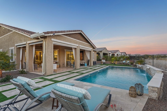 pool at dusk featuring pool water feature and a patio area