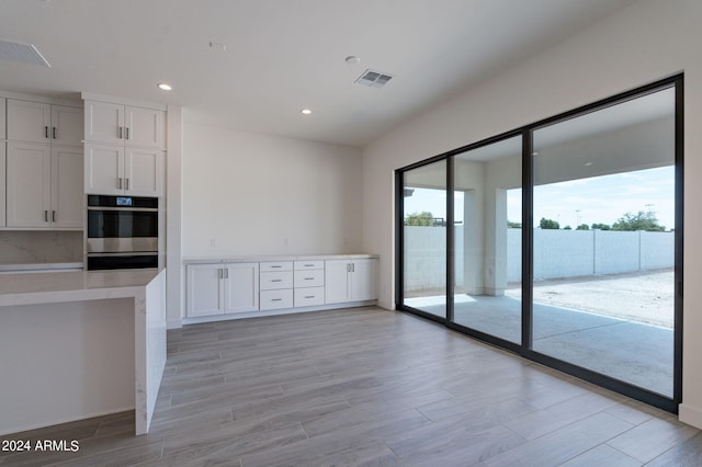 kitchen featuring white cabinets, double oven, and tasteful backsplash