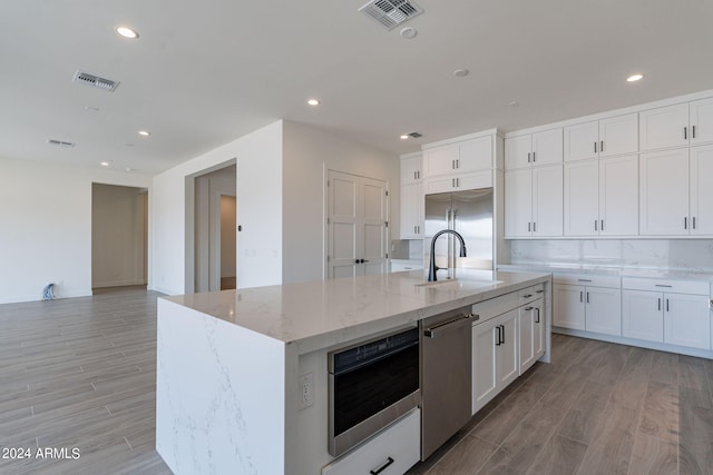 kitchen featuring white cabinetry, sink, light stone countertops, a kitchen island with sink, and appliances with stainless steel finishes