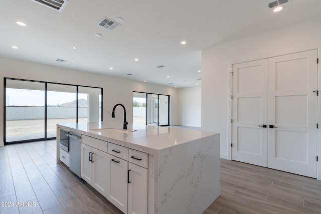 kitchen featuring dishwasher, a center island with sink, white cabinets, sink, and light stone countertops