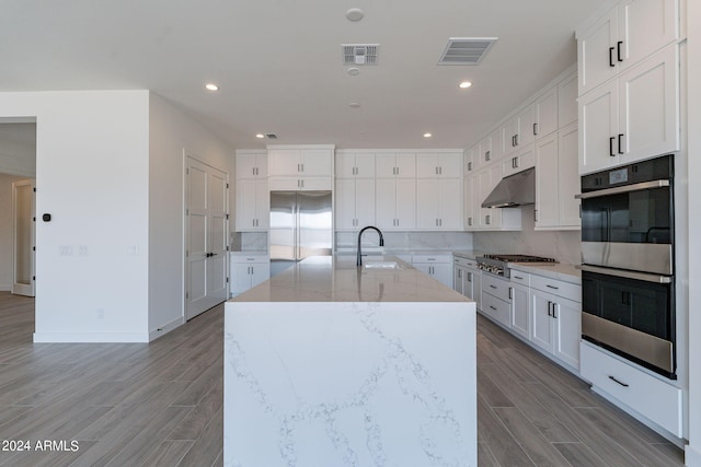 kitchen with a kitchen island with sink, white cabinets, sink, light stone countertops, and appliances with stainless steel finishes