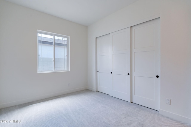 unfurnished bedroom with light colored carpet and a closet