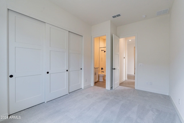 unfurnished bedroom with light colored carpet, connected bathroom, and a closet