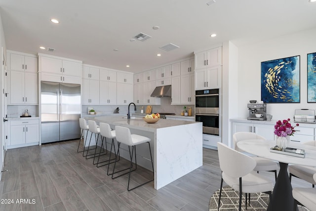 kitchen featuring white cabinetry, stainless steel appliances, decorative backsplash, a kitchen island with sink, and a breakfast bar