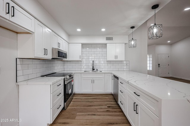 kitchen with sink, kitchen peninsula, pendant lighting, white cabinets, and appliances with stainless steel finishes