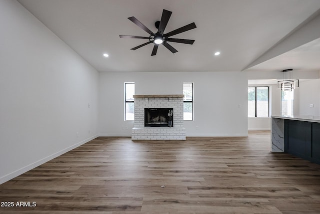 unfurnished living room featuring ceiling fan, light wood-type flooring, a fireplace, and vaulted ceiling