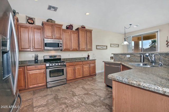 kitchen with hanging light fixtures, appliances with stainless steel finishes, sink, and dark stone countertops