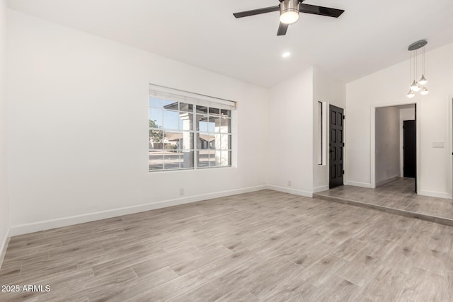 empty room with baseboards, a ceiling fan, light wood finished floors, and high vaulted ceiling