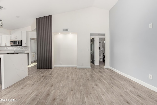 unfurnished living room featuring visible vents, light wood finished floors, baseboards, and high vaulted ceiling