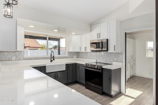 kitchen with appliances with stainless steel finishes, a sink, light wood finished floors, lofted ceiling, and backsplash