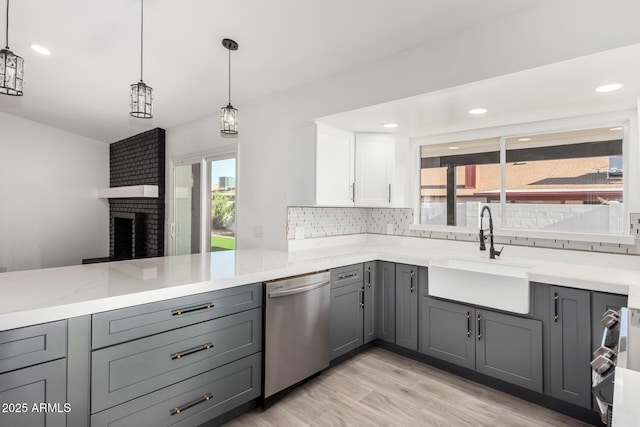 kitchen with stainless steel dishwasher, light stone countertops, tasteful backsplash, a sink, and gray cabinetry