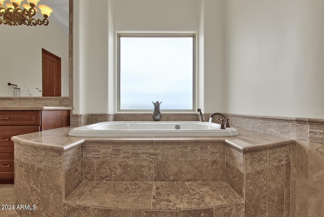 bathroom with a notable chandelier and tiled bath