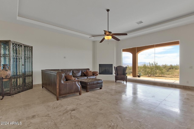 living room with light tile floors, a tray ceiling, and ceiling fan