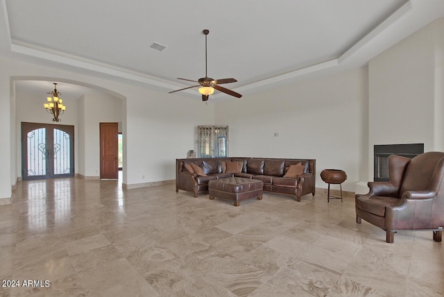 tiled living room featuring french doors, ceiling fan with notable chandelier, and a tray ceiling