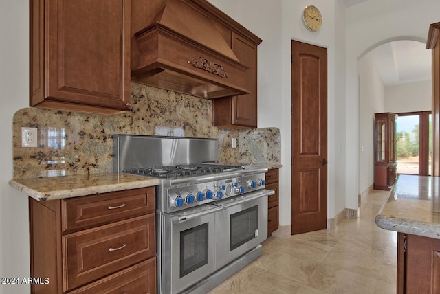 kitchen featuring light tile floors, custom exhaust hood, range with two ovens, backsplash, and light stone counters