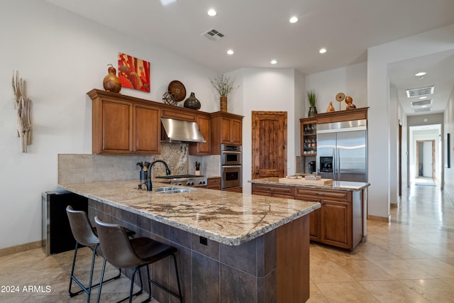 kitchen featuring kitchen peninsula, backsplash, appliances with stainless steel finishes, range hood, and a breakfast bar area