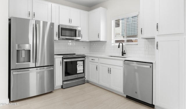 kitchen featuring a sink, stainless steel appliances, white cabinetry, light countertops, and decorative backsplash