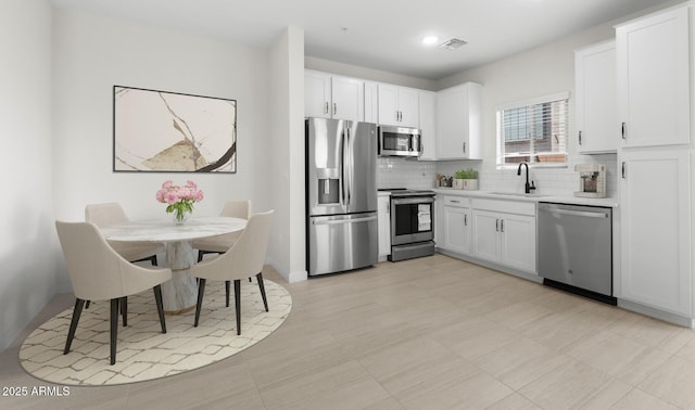 kitchen featuring a sink, white cabinetry, decorative backsplash, light countertops, and appliances with stainless steel finishes