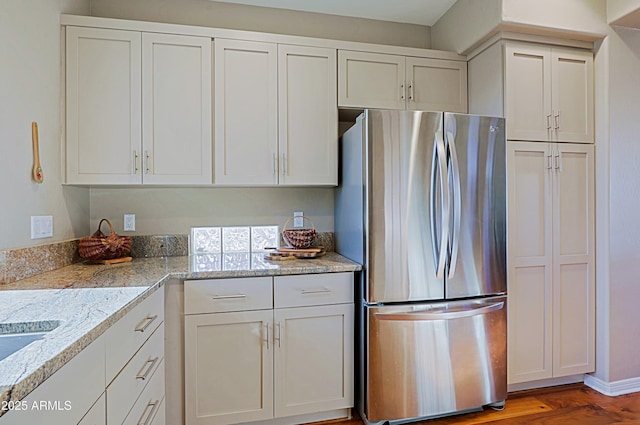 kitchen with white cabinets, light stone counters, wood finished floors, and freestanding refrigerator