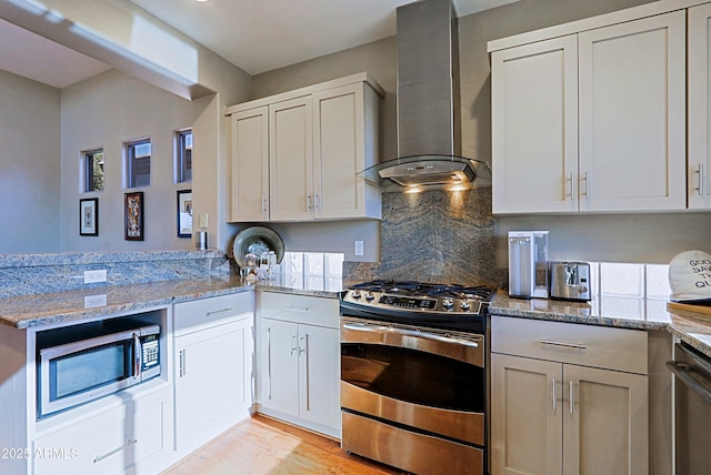 kitchen with light wood finished floors, backsplash, wall chimney range hood, light stone countertops, and stainless steel appliances