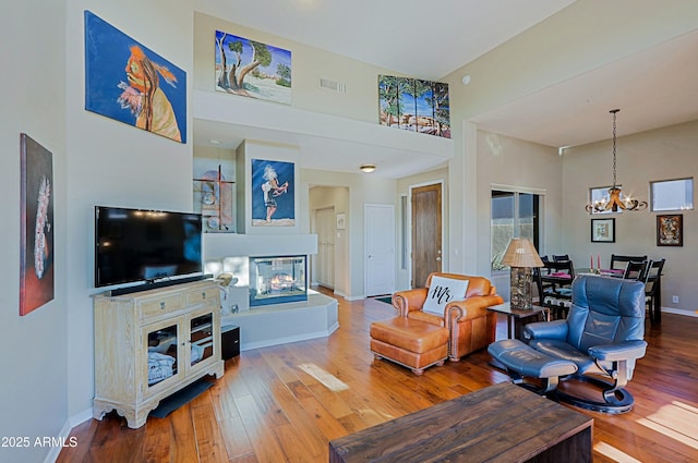 living room featuring a towering ceiling, baseboards, a multi sided fireplace, and wood-type flooring